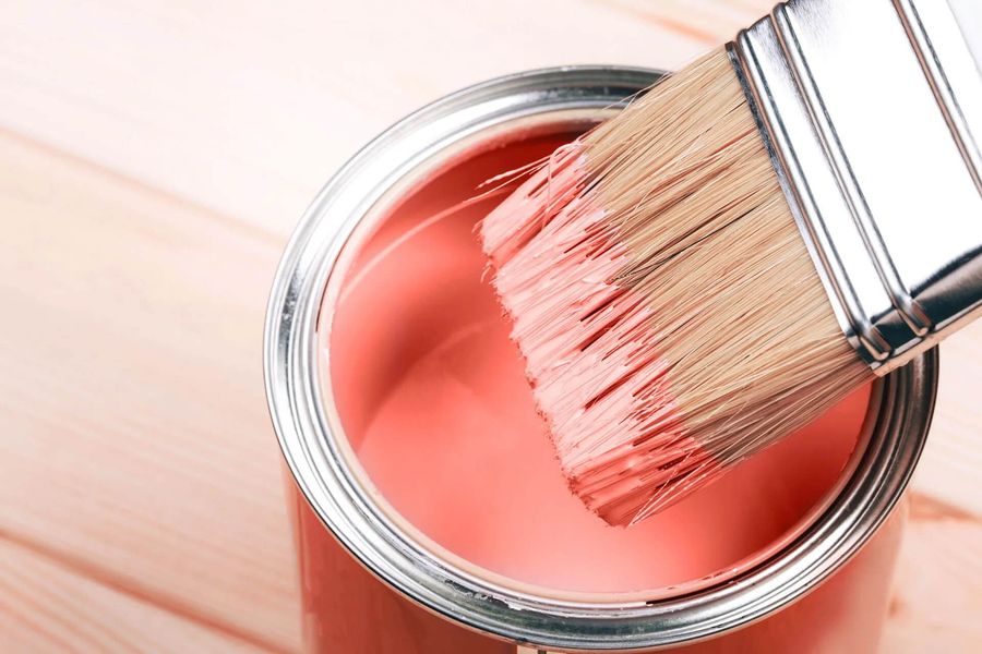 Pinsel mit rosafarbener Farbe taucht in offene Farbdose auf hellem Holzuntergrund.